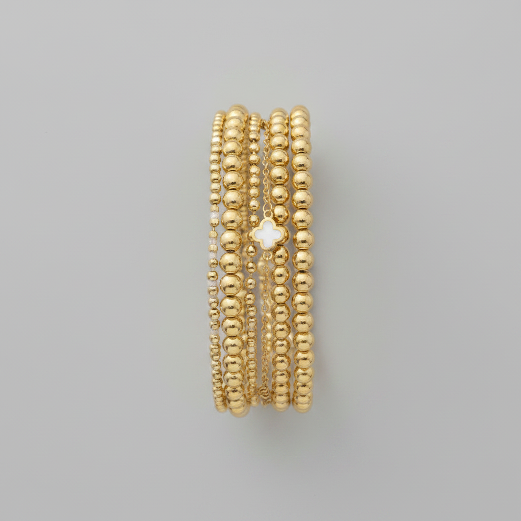 Gold beaded bracelet stack flat lay on light gray background